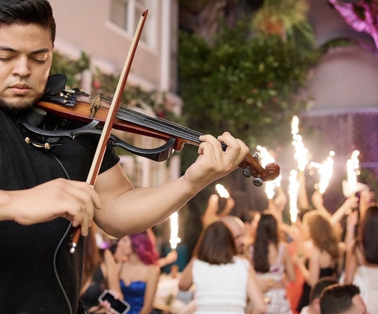 Musician playing violin at a concert with crowd of audience members in background with raised hands