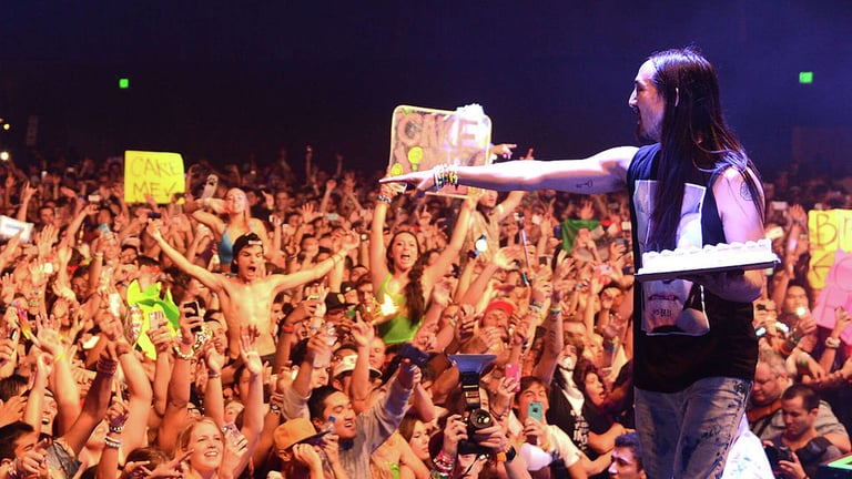 Performer on stage reaching toward enthusiastic crowd with raised hands at concert venue