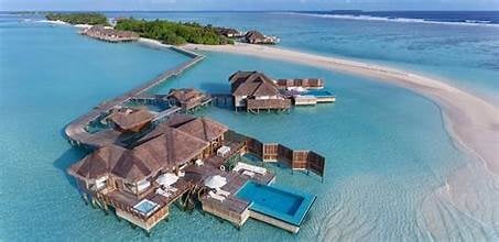 Aerial view of overwater bungalows and villas in turquoise lagoon with sandy island in background