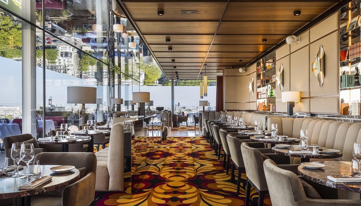 Modern upscale restaurant interior with booth seating, geometric patterned carpet, large windows, and elegant table settings