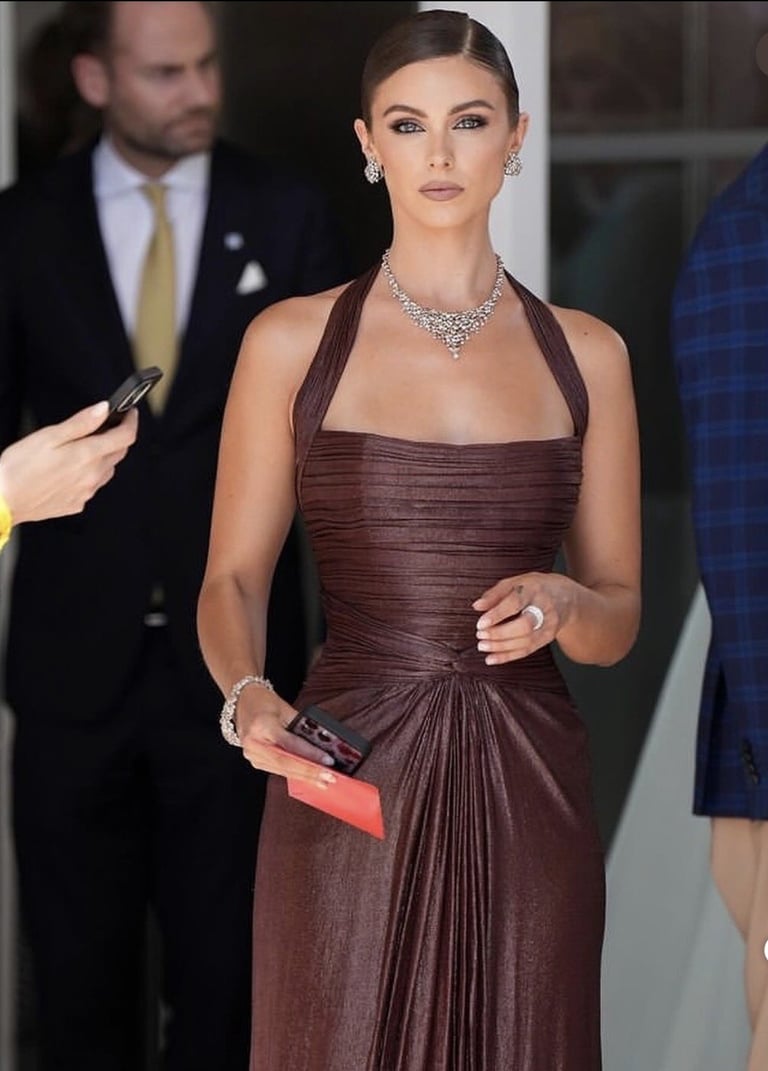 Woman in burgundy pleated halter gown with diamond necklace and bracelet at formal event, holding clutch