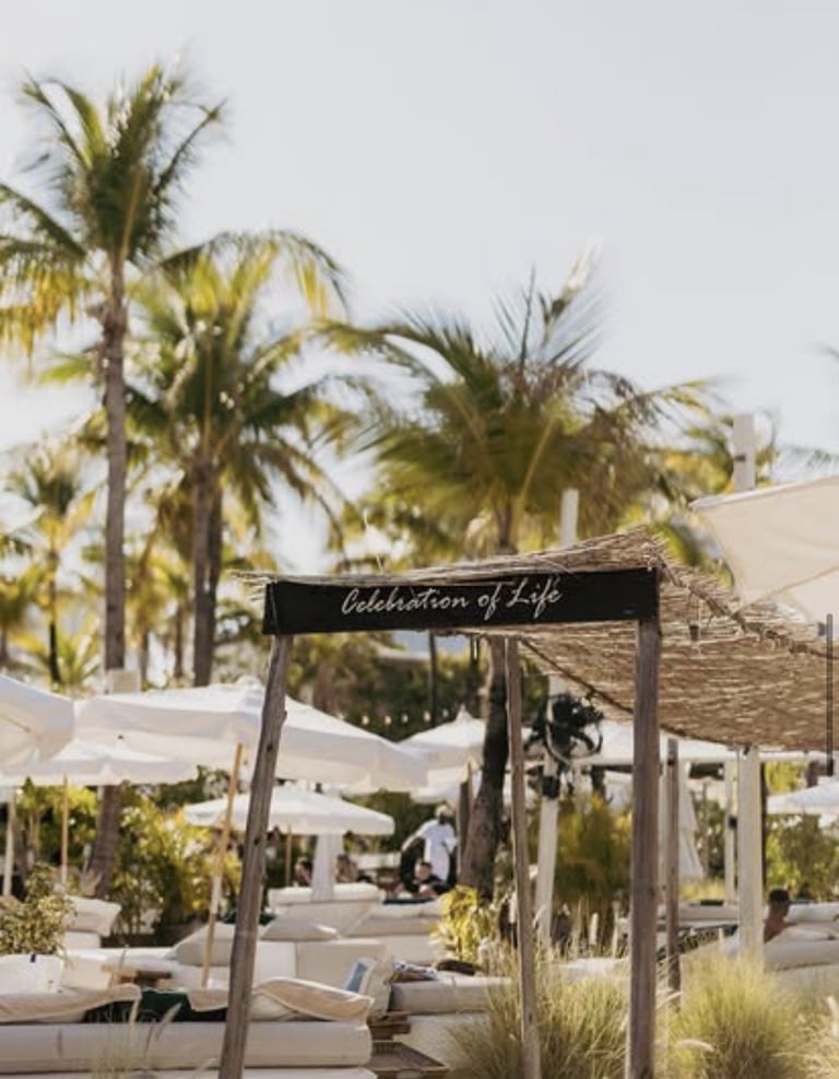 Wooden archway with Celebration of Life sign at outdoor event venue with palm trees and white seating
