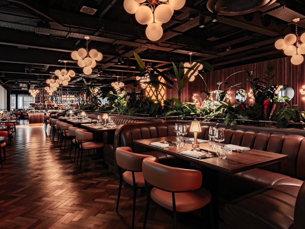 Modern upscale restaurant interior with burgundy leather booth seating, wooden tables, ambient lighting from decorative globe fixtures, and potted plants