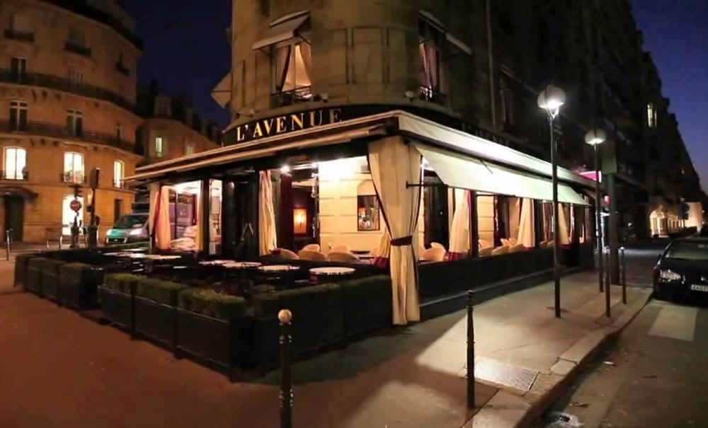 LAvenir restaurant storefront lit up at night on a Paris street corner with classical buildings in background