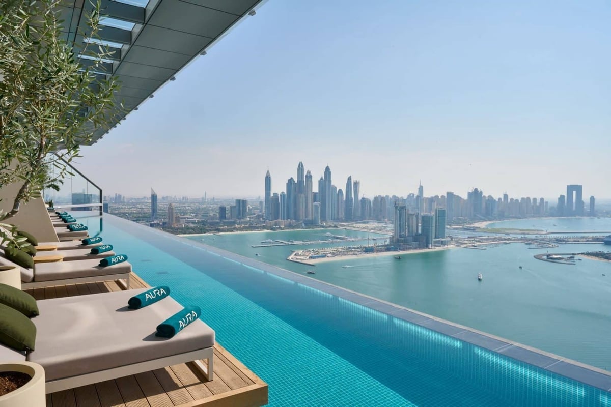 Luxury rooftop infinity pool overlooking Dubai Marina skyline and coastline with lounge chairs and calm turquoise waters