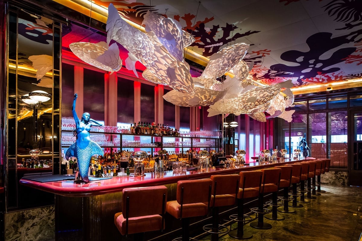 Modern bar interior with ornate crystal pendant lights, long wooden counter with red neon accents, and blue silhouette sculpture