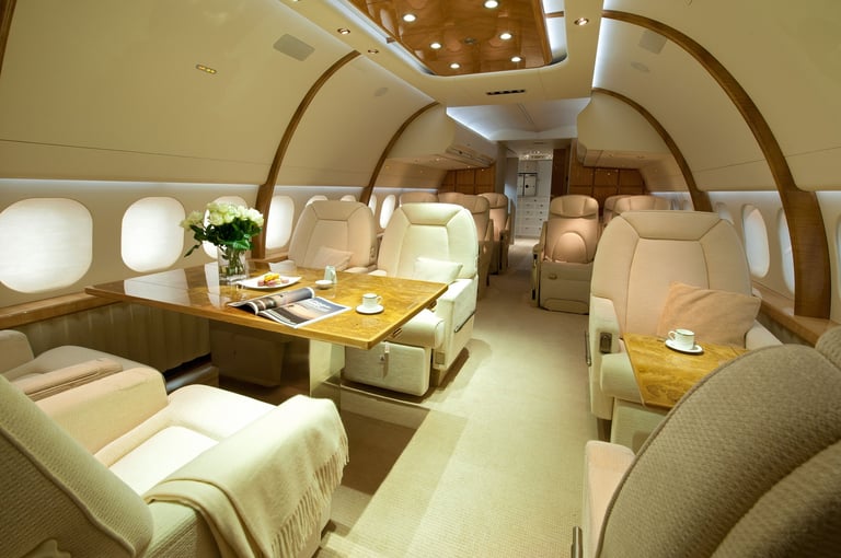 Luxurious private jet interior with cream-colored seating, wood paneling, conference table with place settings, and arched cabin design