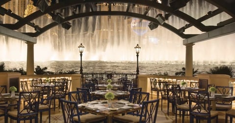 Elegant rooftop dining area with wooden tables and chairs under a pergola, overlooking a cityscape at sunset