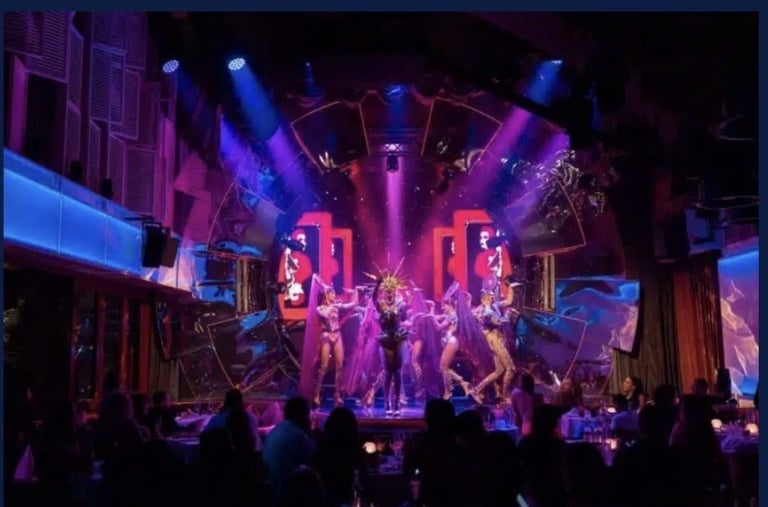 Live concert stage with performers dancing under vibrant purple and blue lighting, audience members visible in foreground
