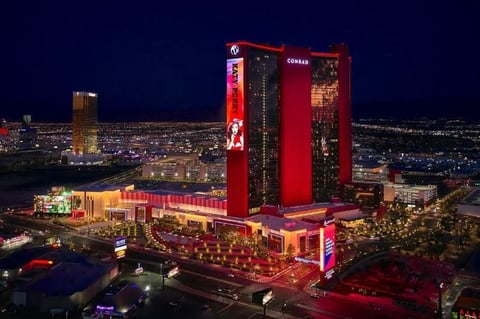 Aerial view of a large red-lit casino resort at night with surrounding buildings and city lights in the background