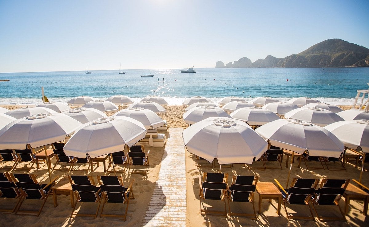 Beach resort with rows of white umbrellas and lounge chairs overlooking turquoise water and distant islands
