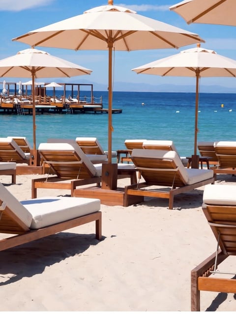 Luxury beach club with wooden lounge chairs, cream umbrellas, and turquoise Mediterranean sea view