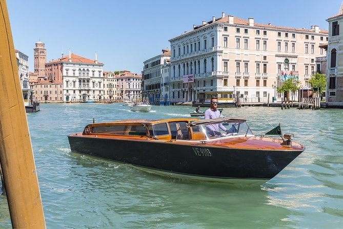 Black and brown motorboat on the turquoise waters of Venice's Grand Canal with historic Venetian buildings lining the waterway