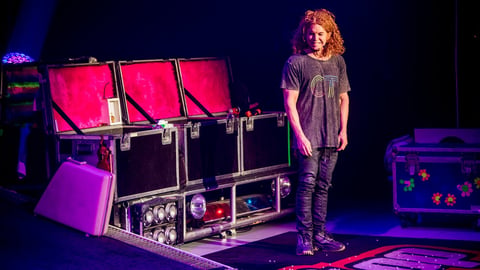 Young performer on stage with elaborate lighting rig and equipment in dark venue with pink and purple stage lighting