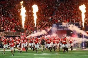 Football team running onto field with pyrotechnics and flames during stadium entrance ceremony