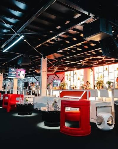Modern exhibition space with red sculptural seating pods, track lighting, and display areas in an industrial venue