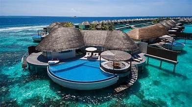 Aerial view of luxury overwater bungalows with thatched roofs and blue pools in a turquoise tropical lagoon
