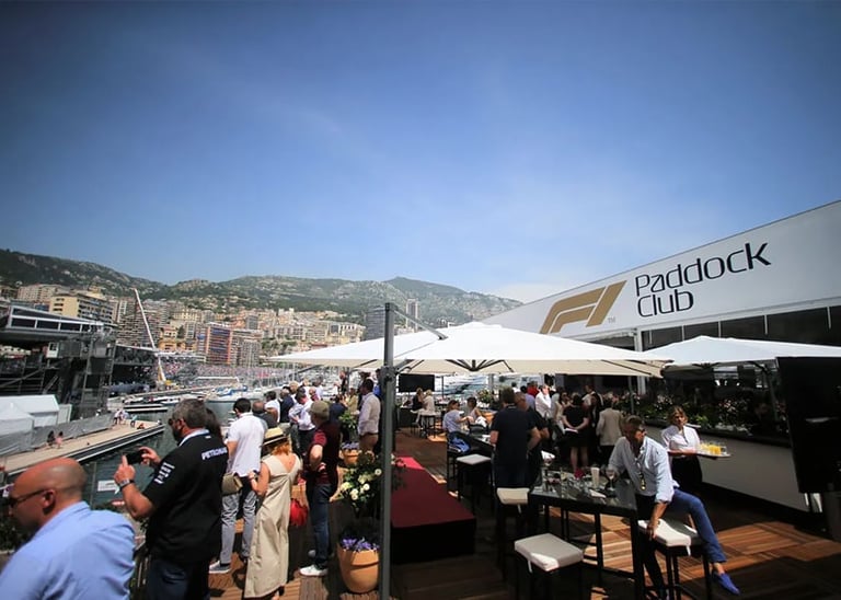 Crowded outdoor event at Paddock Club with white umbrellas, Mediterranean hillside landscape in background