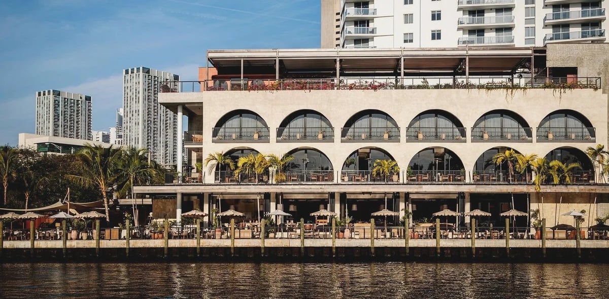 Waterfront building with distinctive arched windows, outdoor dining area, and city skyline
