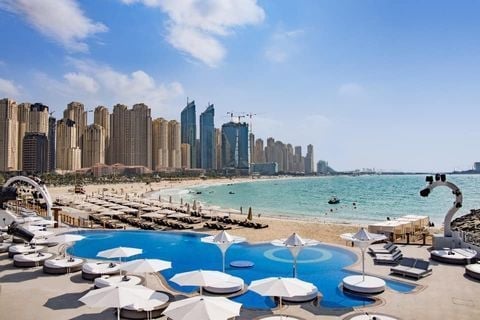 Beach resort with blue umbrellas and loungers overlooking turquoise water and high-rise buildings in a coastal city