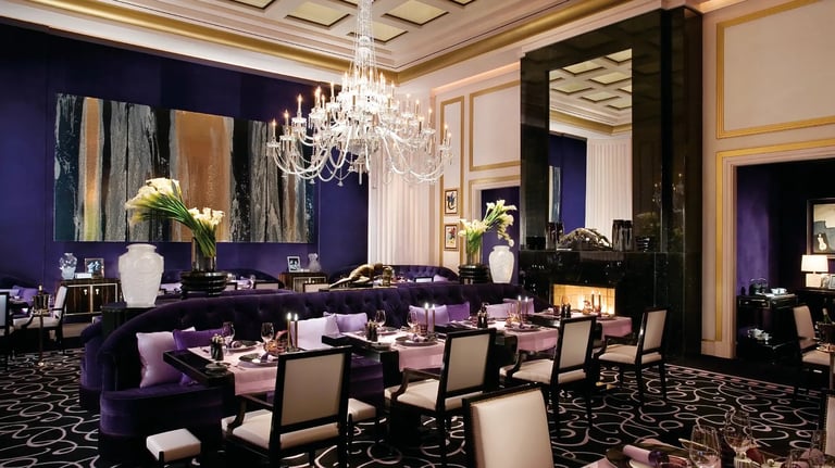 Elegant fine dining restaurant with navy walls, crystal chandelier, purple upholstered banquettes, white place settings, and gold accents