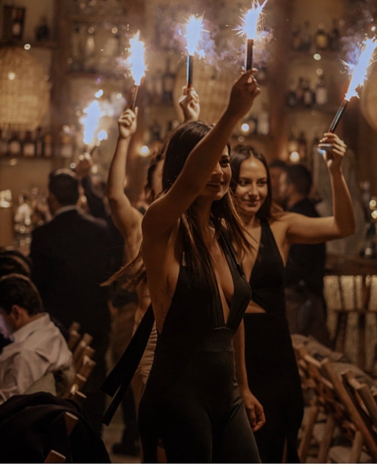 Group of people at a party holding lit sparklers in a dimly lit venue with warm lighting