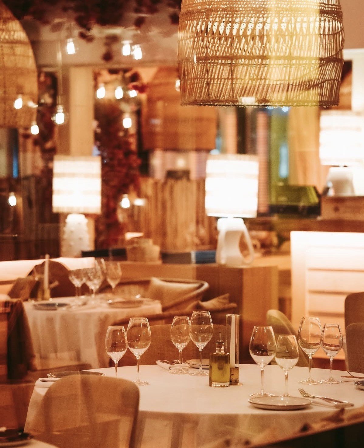 Elegant restaurant dining room with woven pendant lamp, wine glasses, place settings, and warm ambient lighting