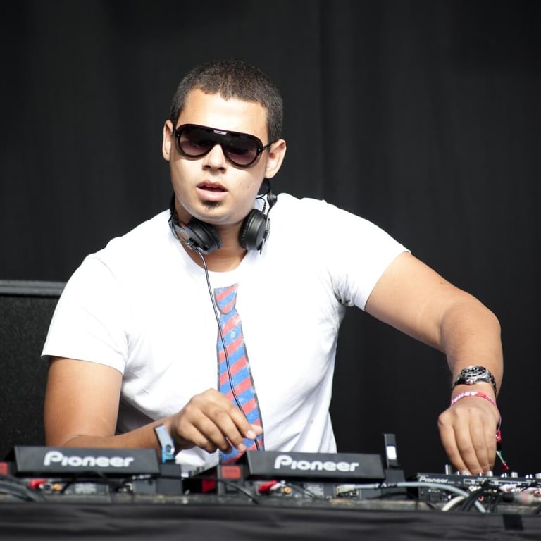 DJ in white t-shirt and sunglasses performing at Pioneer turntables against dark background