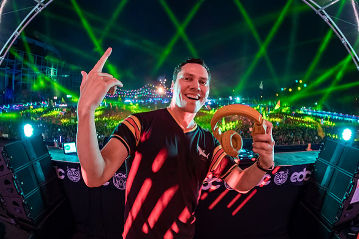 DJ at music festival holding oversized pretzels, smiling with green laser lights and crowd in background