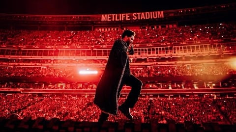 Performer in black coat on stage at Metlife Stadium with crowd illuminated by red lights