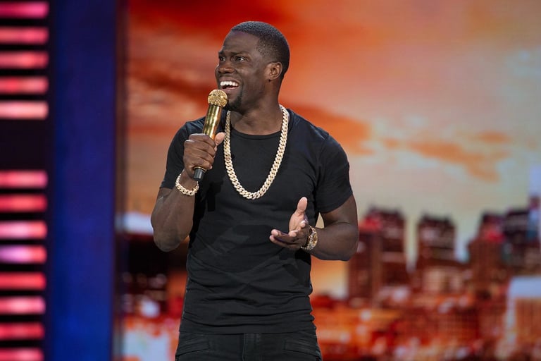 Man performing on stage with microphone, wearing black shirt and chain necklace against cityscape backdrop