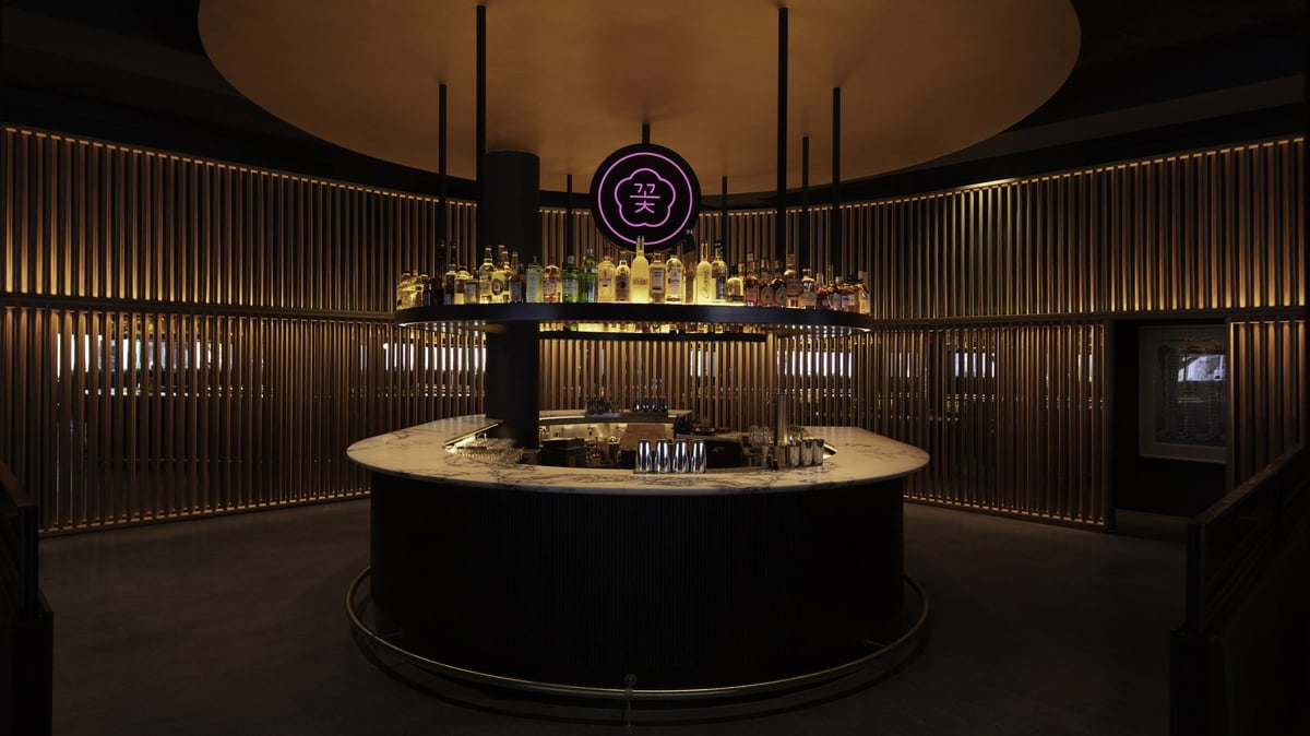 Modern luxury bar interior with circular counter, pendant lighting, vertical slat panels, and dark ambiance