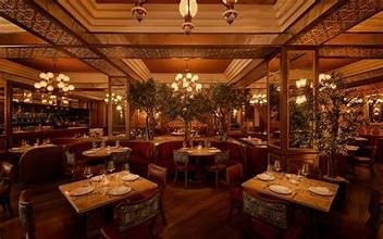 Luxurious upscale restaurant dining room with warm wood paneling, crystal chandeliers, round tables, burgundy seating, and elegant gold accents
