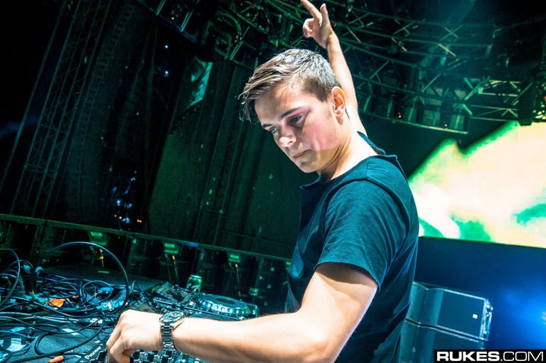 Young male DJ performing at a turntable with headphones, colored stage lighting in background