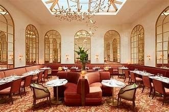 Elegant restaurant interior with burgundy seating, arched windows, crystal chandelier, and round tables arranged in a circular room