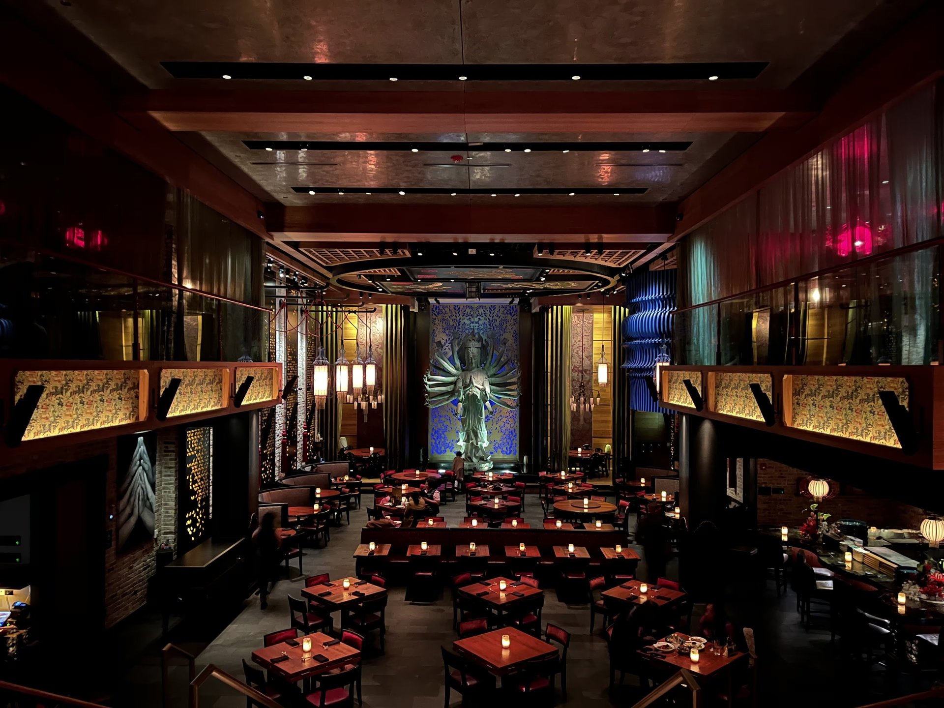 Upscale restaurant interior with ambient lighting, candlelit tables, wooden beams, and ornate gold-accented wall displays