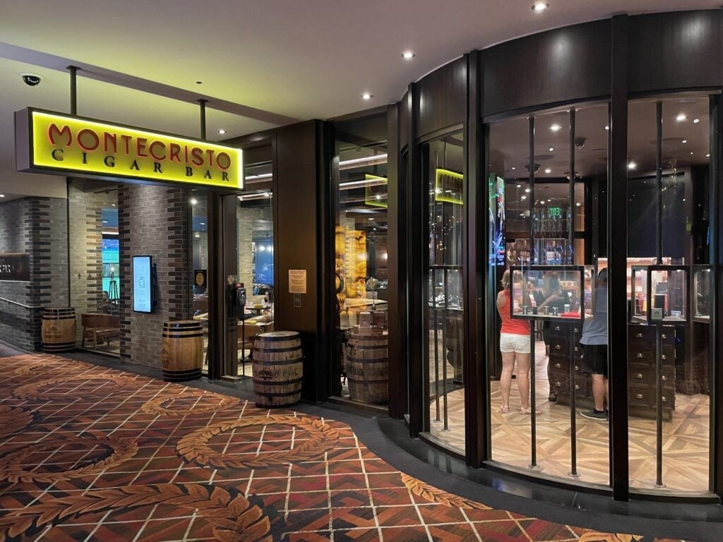 Luxury retail storefronts in a mall corridor, featuring Montecristo shop with yellow signage and dark modern storefront displays
