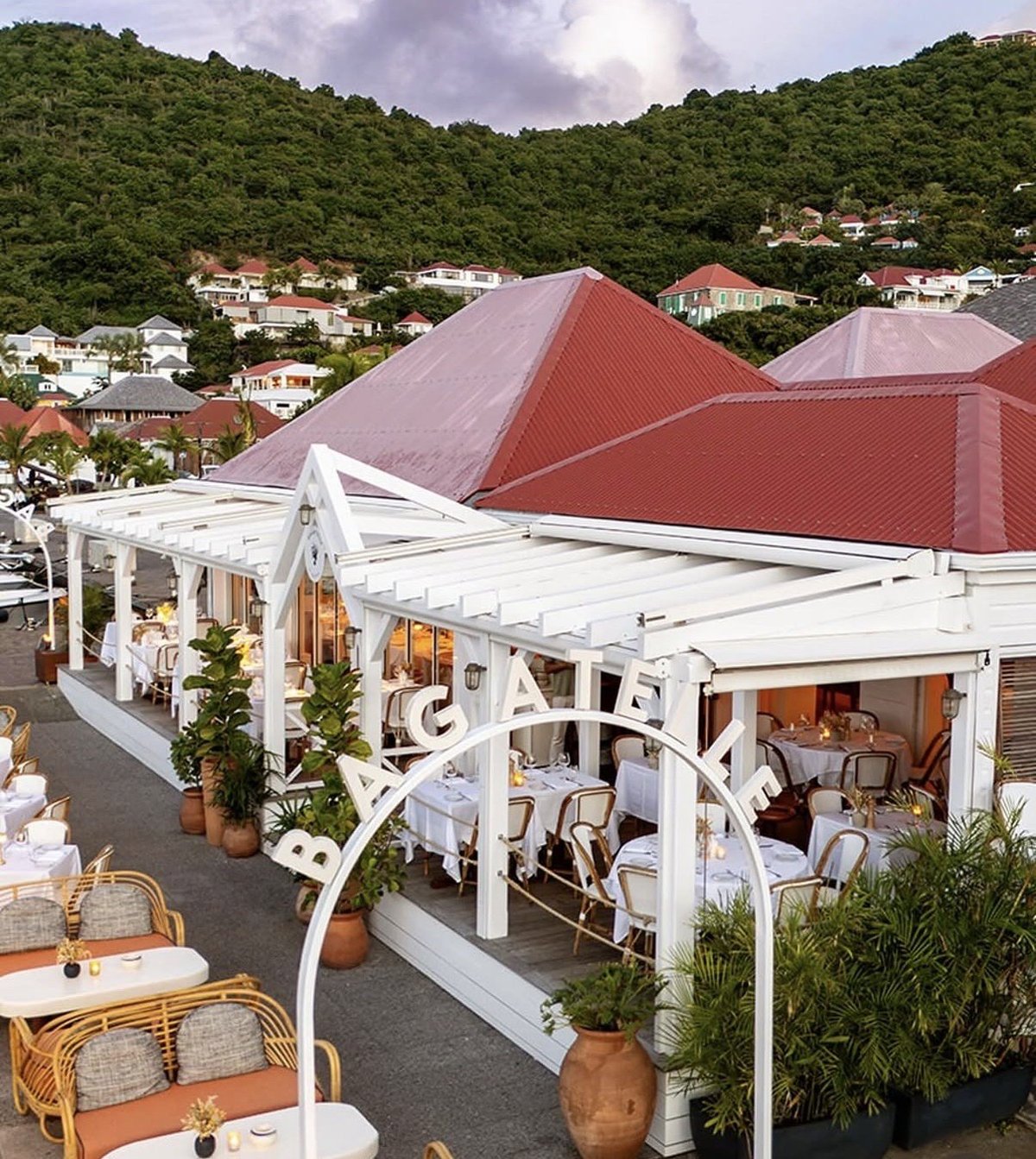 Modern white pergola structure with seating area overlooking hillside homes with red metal roofs and lush green vegetation