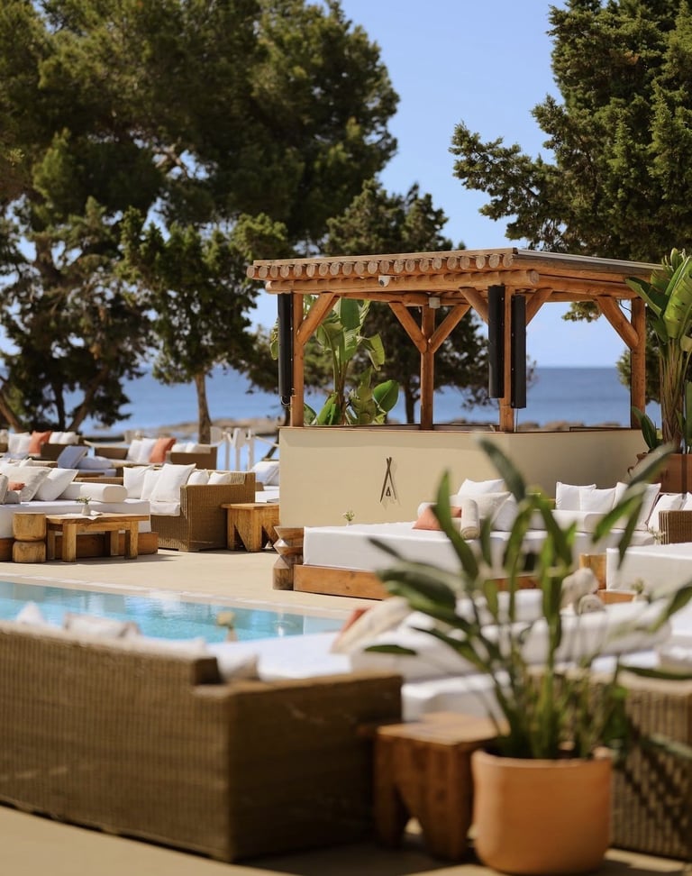 Luxury beachfront poolside lounge with wooden pergola, loungers, potted plants, and sea view under clear sky