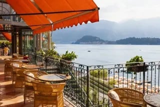 Waterfront terrace with orange umbrella overlooking a calm bay with mountains in the distance
