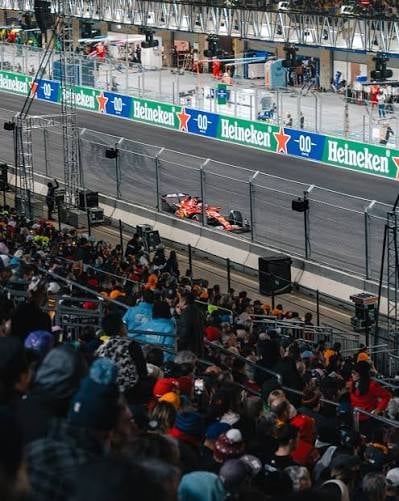 Red Formula 1 car on track with Heineken advertising boards, surrounded by spectators and support vehicles at a race event