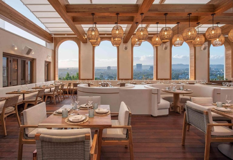 Upscale restaurant dining room with wooden beams, large windows overlooking mountains, pendant lighting, and table settings