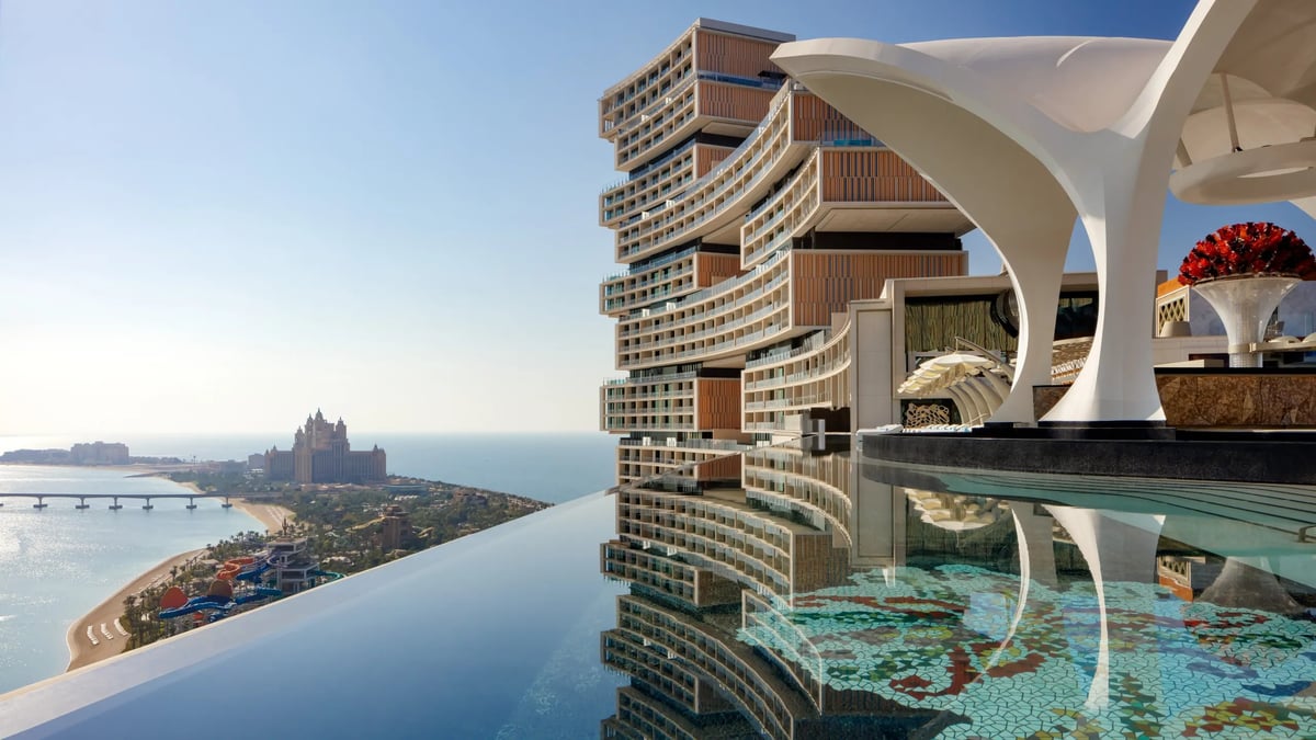 Modern luxury high-rise residential tower with infinity pool overlooking a coastal city skyline and waterfront