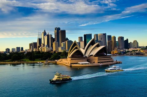 Sydney Opera House and harbor with city skyline, ferries, and blue water under a clear sky