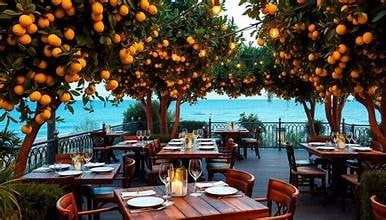 Outdoor restaurant terrace shaded by orange citrus trees with sea view and dining tables set for service
