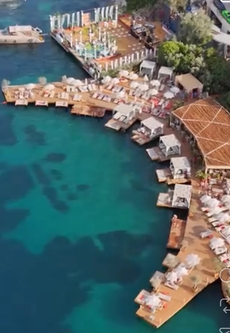 Aerial view of a Mediterranean waterfront with turquoise water, residential buildings, and wooden docks with boats