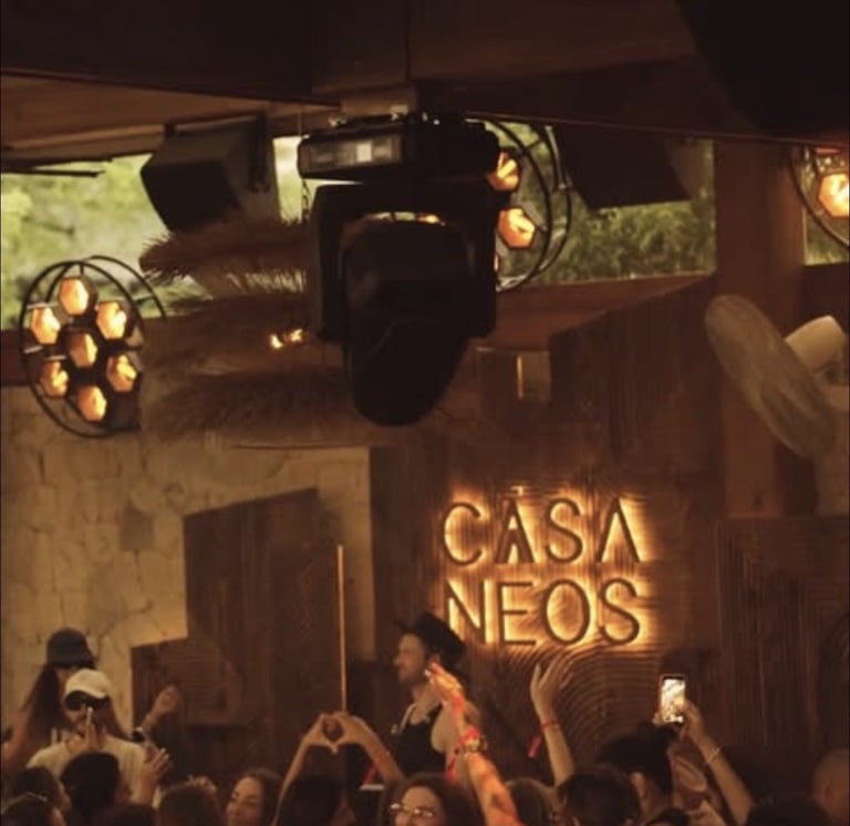 Interior of Casa Neos nightclub with stage lighting rigs and crowd below illuminated signage