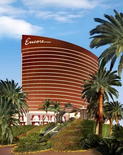 Encore Hotel Las Vegas, a curved red building with white horizontal lines, surrounded by palm trees under blue sky