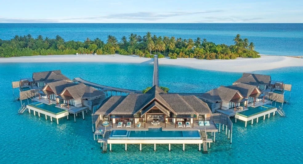 Aerial view of luxury overwater bungalows with central villa on turquoise lagoon and tropical island in background