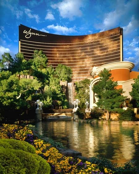 Wynn Hotel and Casino in Las Vegas with distinctive curved gold facade overlooking a pond with lush landscaping